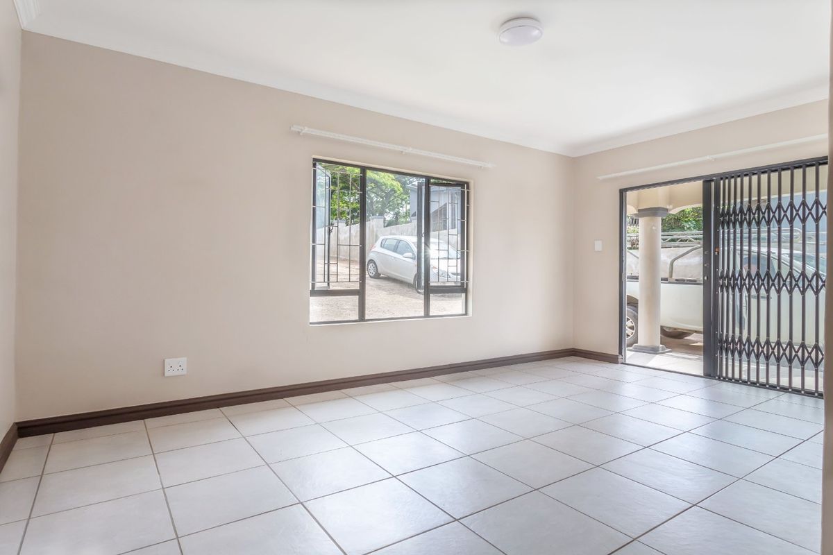 A bright, empty living room featuring neutral walls, tiled flooring, and a security gate leading to the exterior.