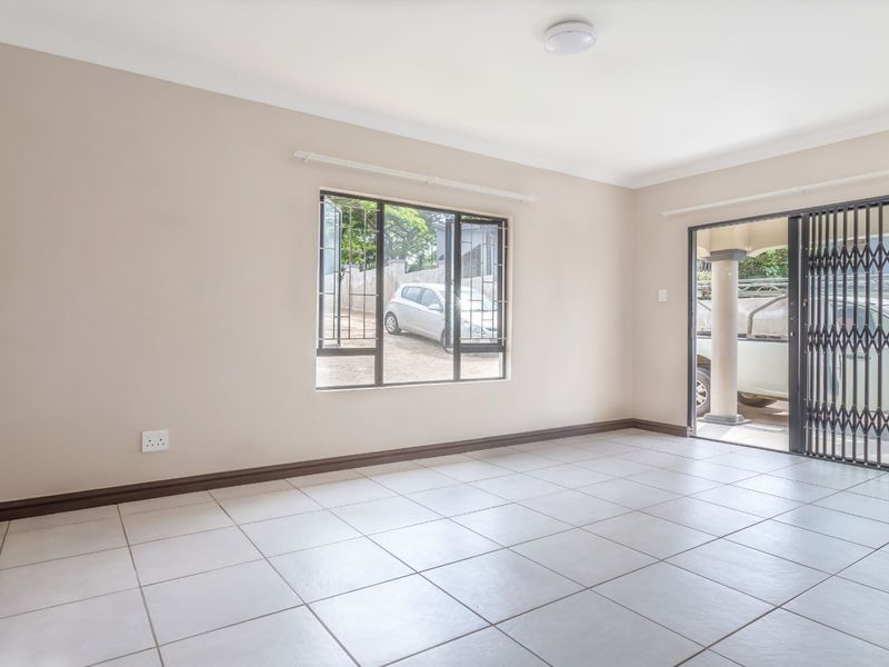 A bright, empty living room featuring neutral walls, tiled flooring, and a security gate leading to the exterior.