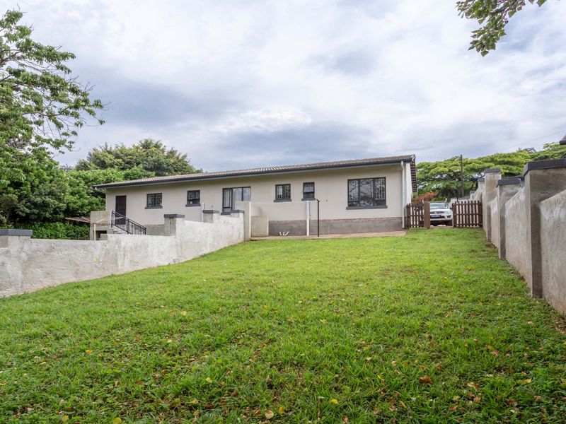 Rear view of the townhouse featuring a spacious lawn, concrete boundary walls, and a paved patio area with security-fitted windows.