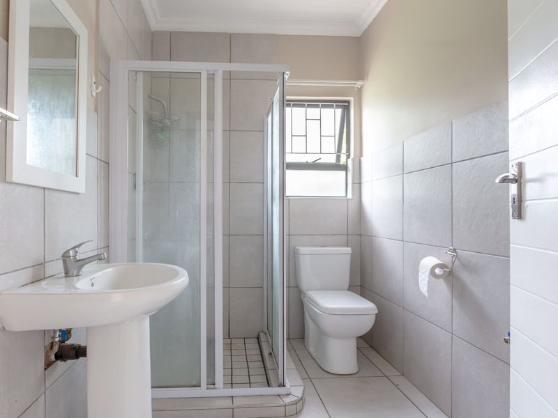 A functional bathroom featuring a pedestal basin, a shower enclosure, and a toilet, finished with neutral wall and floor tiles.