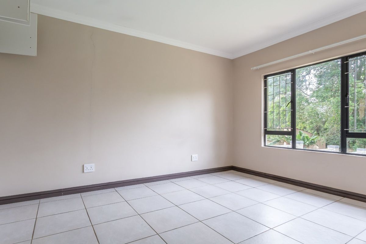 An empty bedroom featuring neutral wall paint, tiled flooring, and a window fitted with security bars.