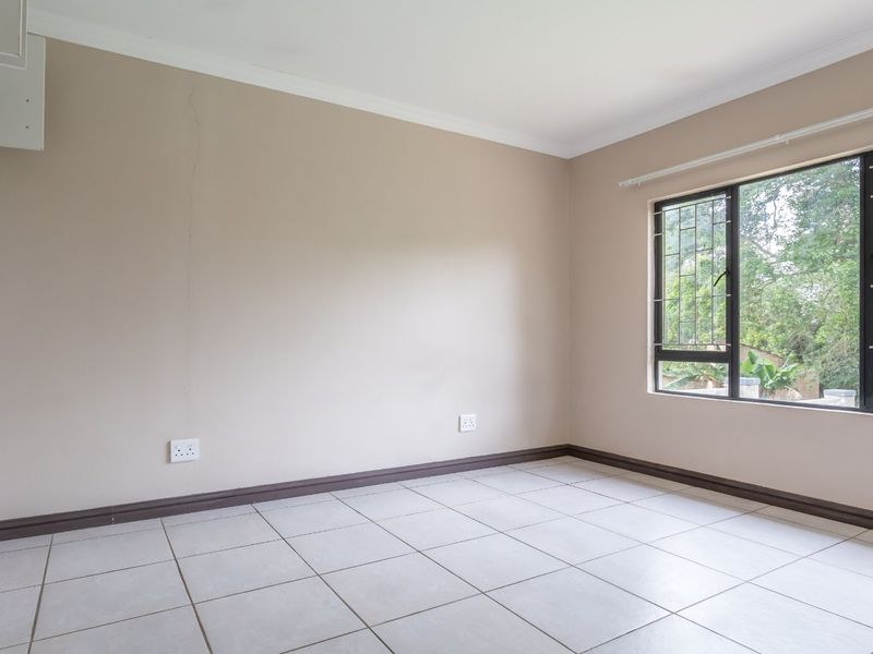 An empty bedroom featuring neutral wall paint, tiled flooring, and a window fitted with security bars.