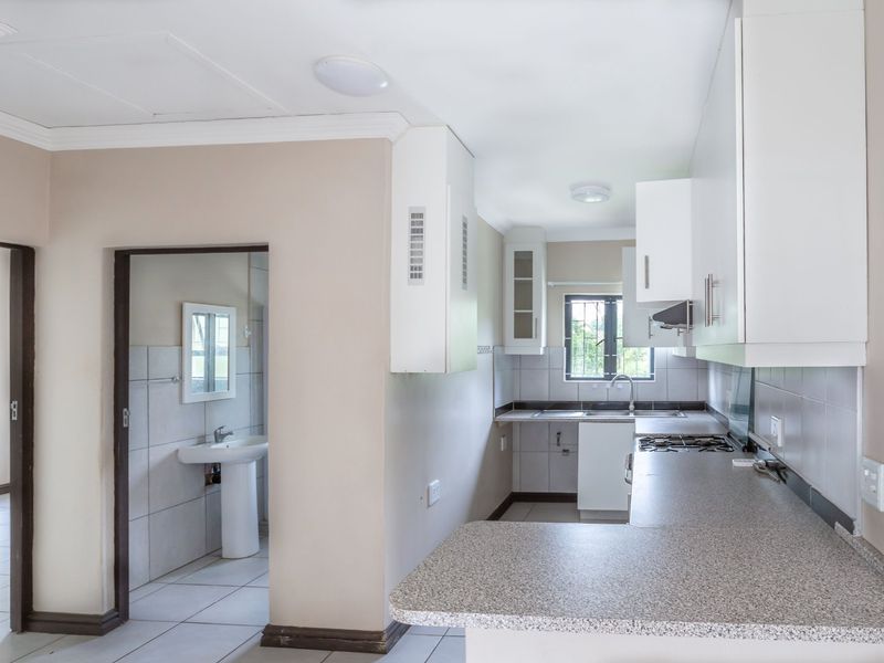 A functional kitchen featuring white cabinetry, laminate countertops, and a gas hob, with an adjacent bathroom area visible through the doorway.