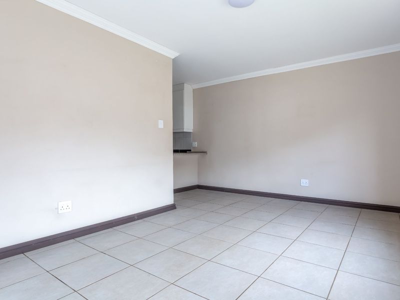 An empty open-plan living area featuring neutral walls, tiled flooring, and coving, with a glimpse of the adjacent kitchen area.