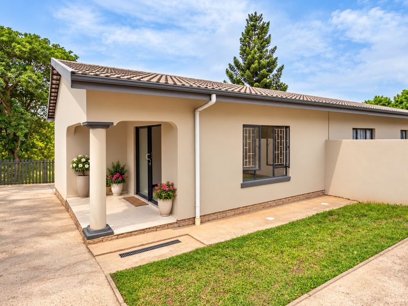 A well-maintained townhouse exterior featuring a covered patio, tiled roof, and neat paved walkway alongside a small garden area.