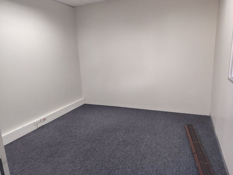 A clean, empty office space featuring neutral walls, grey carpet flooring, and integrated electrical trunking along the baseboards.