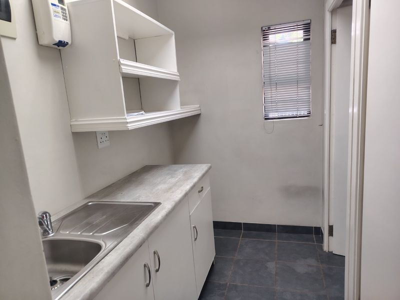A functional scullery area featuring built-in cabinetry, a stainless steel sink, laminate countertops, and tiled flooring, providing practical utility space.