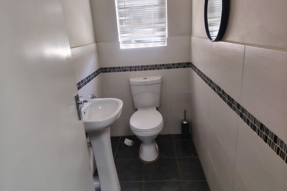 A compact guest bathroom featuring a pedestal basin, toilet, and neutral wall tiling with a decorative mosaic border.