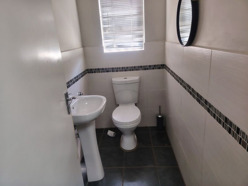 A compact guest bathroom featuring a pedestal basin, toilet, and neutral wall tiling with a decorative mosaic border.