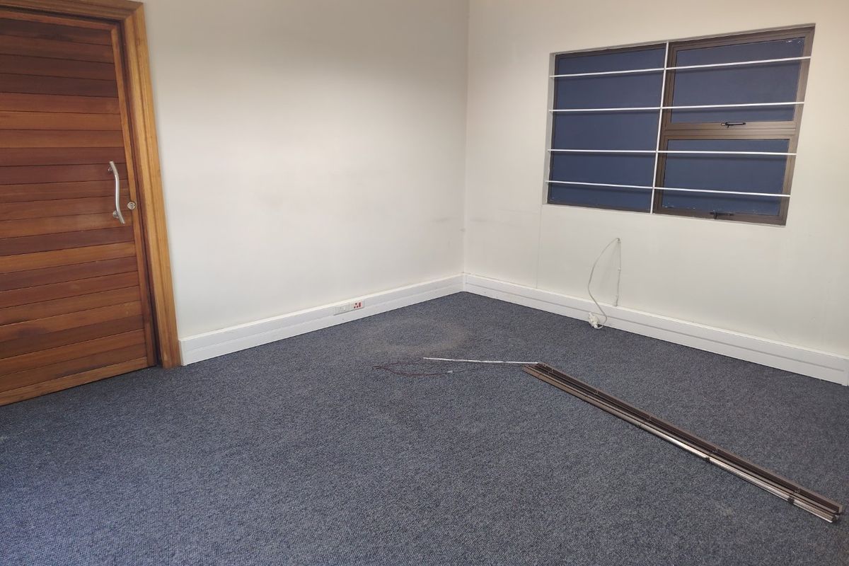 An empty office space featuring carpeted flooring, a timber door, and a window fitted with security bars.