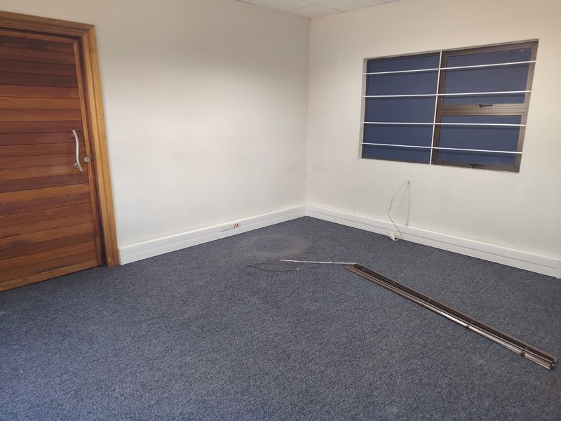 An empty office space featuring carpeted flooring, a timber door, and a window fitted with security bars.