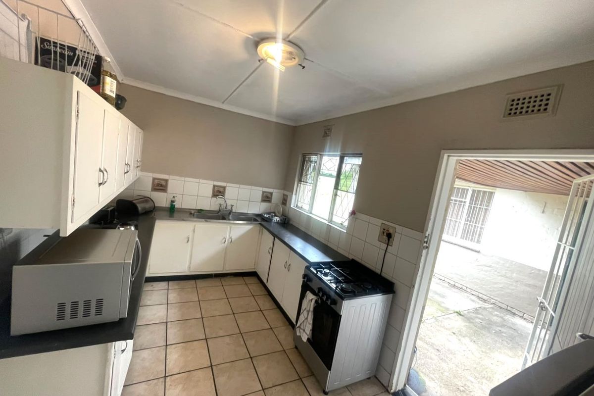 A functional kitchen featuring white cabinetry, tiled flooring, and a freestanding stove, with direct access to an outdoor area through a security door.