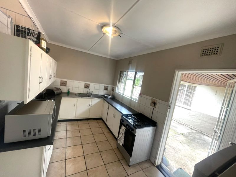 A functional kitchen featuring white cabinetry, tiled flooring, and a freestanding stove, with direct access to an outdoor area through a security door.