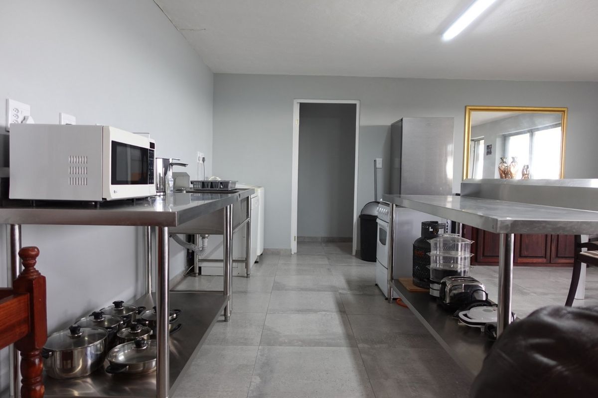 Functional kitchen area featuring stainless steel prep tables, double basin sink, and tiled flooring with neutral wall finishes.