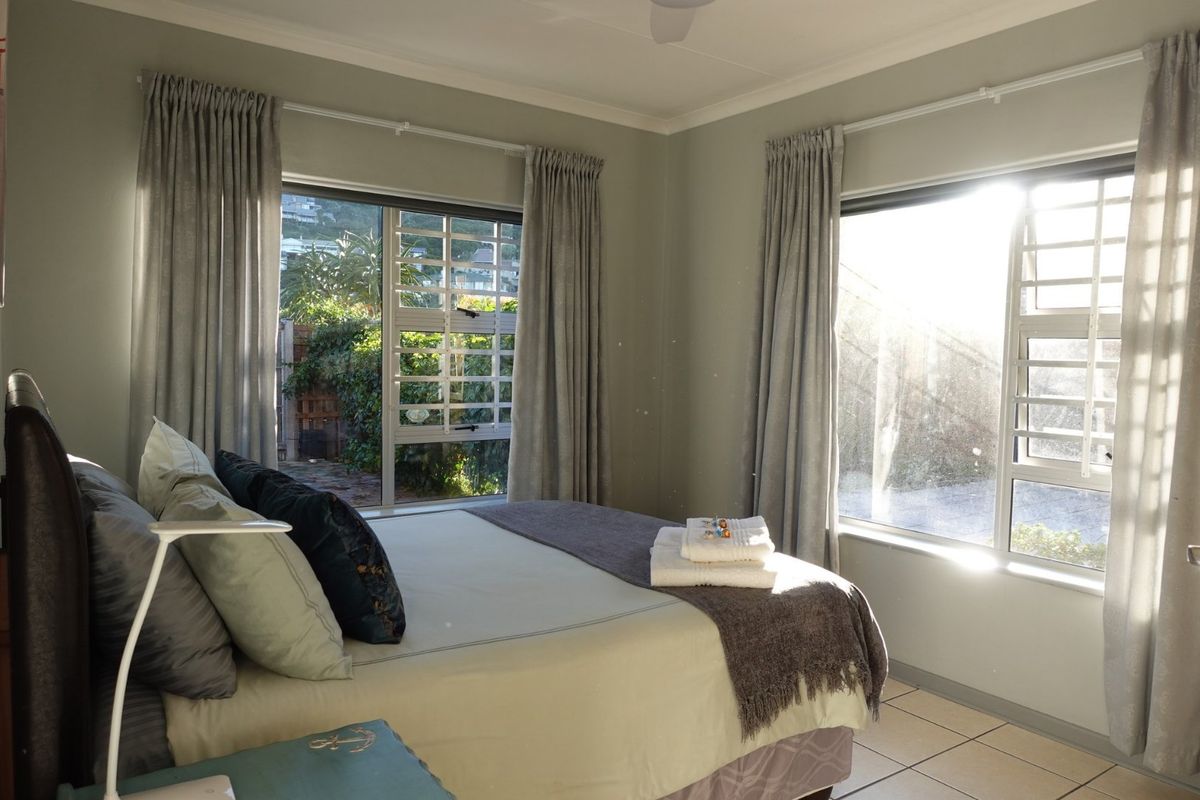 A bright bedroom featuring tiled flooring, large windows with security bars, and neutral wall tones, offering a comfortable and well-maintained living space.