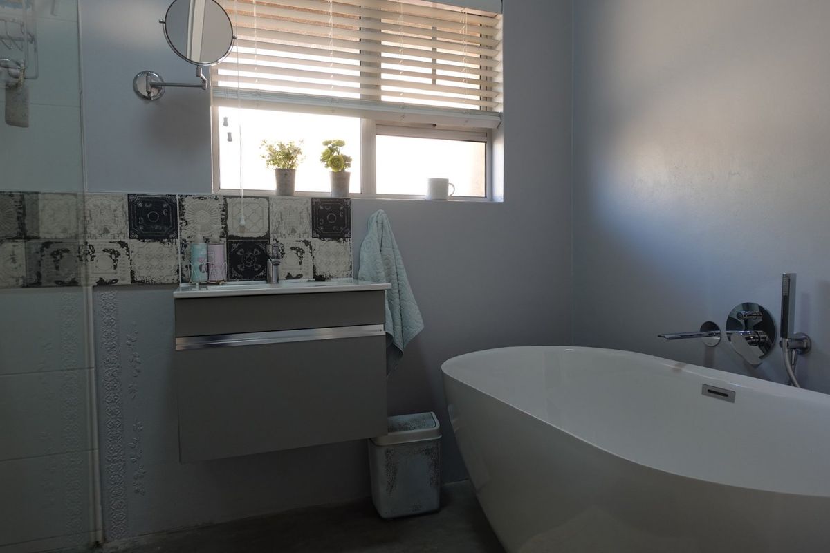 Modern bathroom featuring a sleek freestanding bathtub, wall-mounted fixtures, a contemporary wall-hung vanity, and decorative accent tiling under a window with venetian blinds.