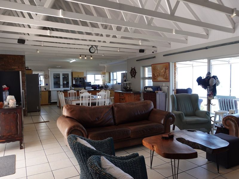 Spacious open-plan living and dining area featuring exposed white timber trusses, tiled flooring, and seamless flow to an outdoor patio through sliding glass doors.