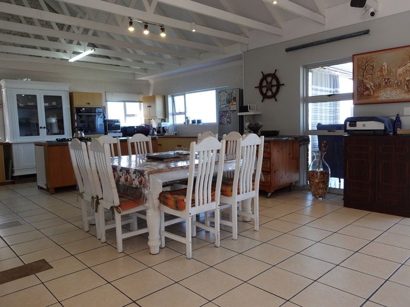 Spacious open-plan kitchen and dining area featuring exposed timber rafters, tiled flooring, and built-in cabinetry with direct access to the outdoor area.