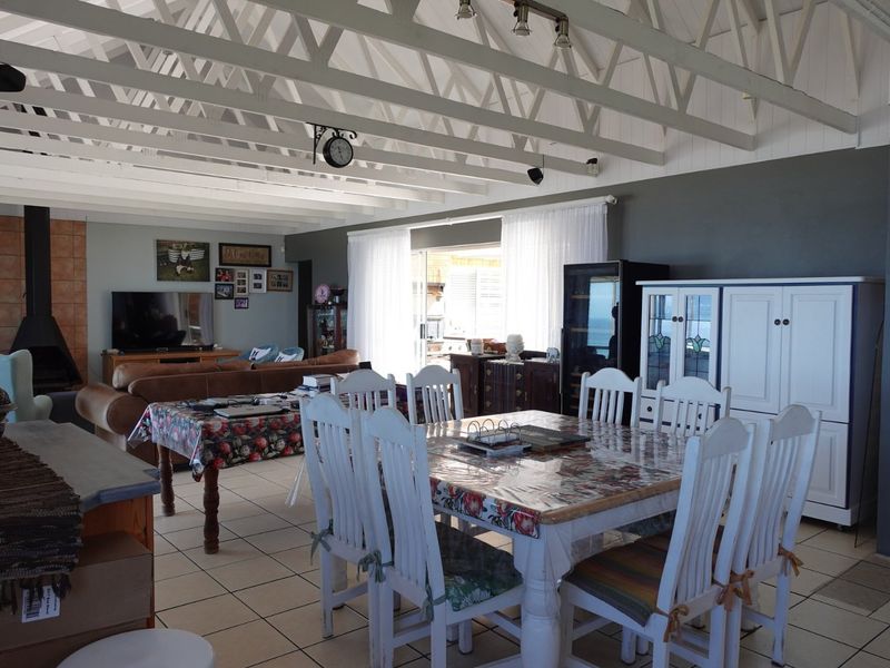 Spacious open-plan living and dining area featuring exposed white timber roof trusses, tiled flooring, and a cozy fireplace with direct access to the patio.