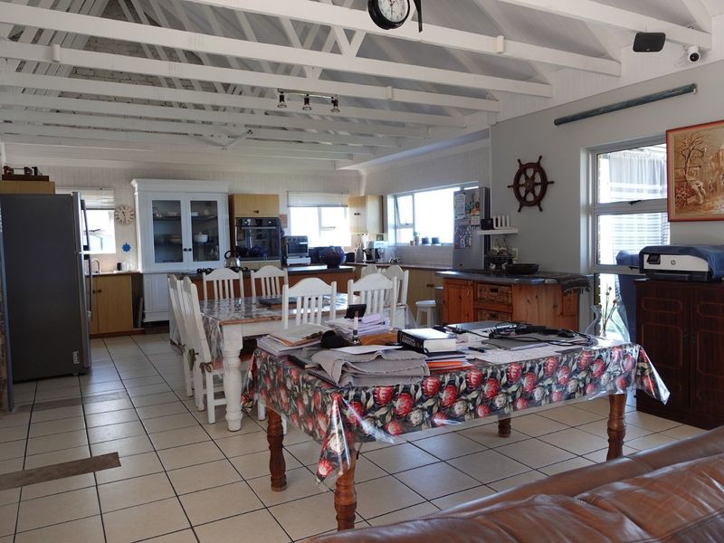 Spacious open-plan living and kitchen area featuring exposed timber ceiling beams, tiled flooring, and a brick fireplace, offering a versatile layout for family living.