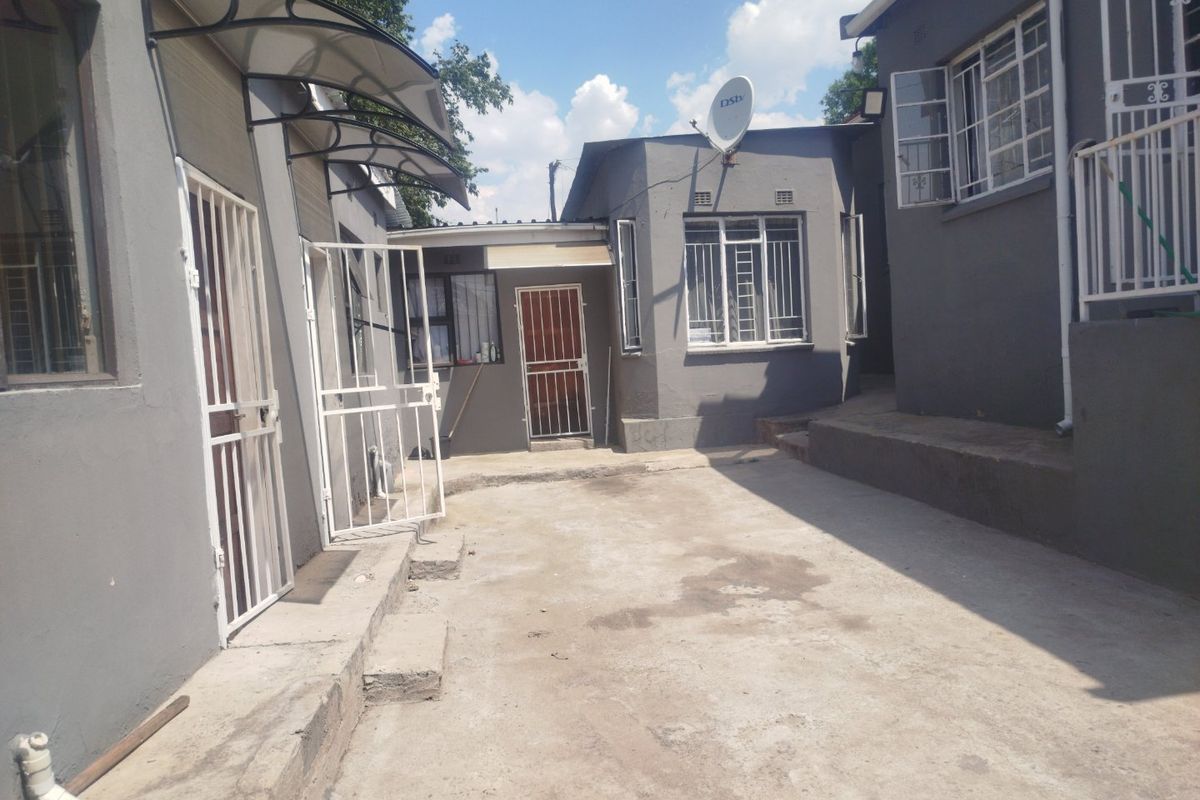 A rear exterior view of the property featuring concrete paving, security gates, burglar bars, and an awning over the entrance.
