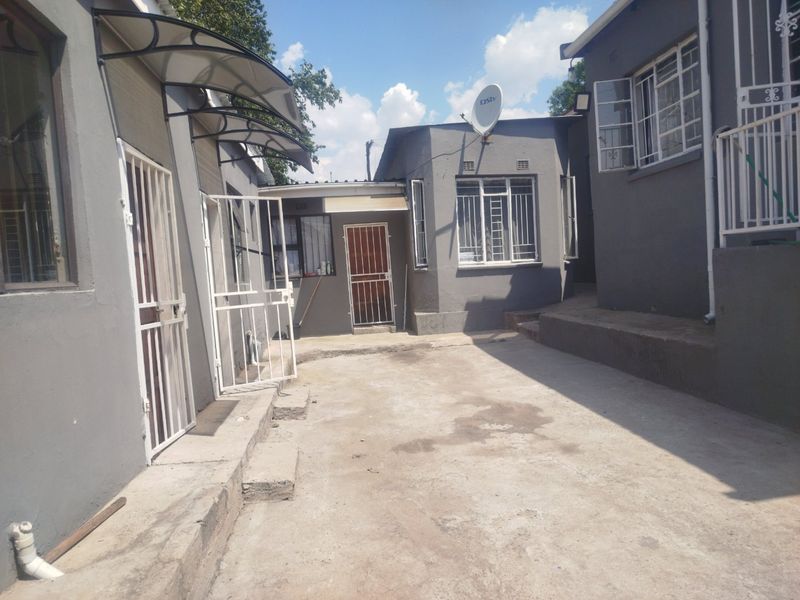 A rear exterior view of the property featuring concrete paving, security gates, burglar bars, and an awning over the entrance.