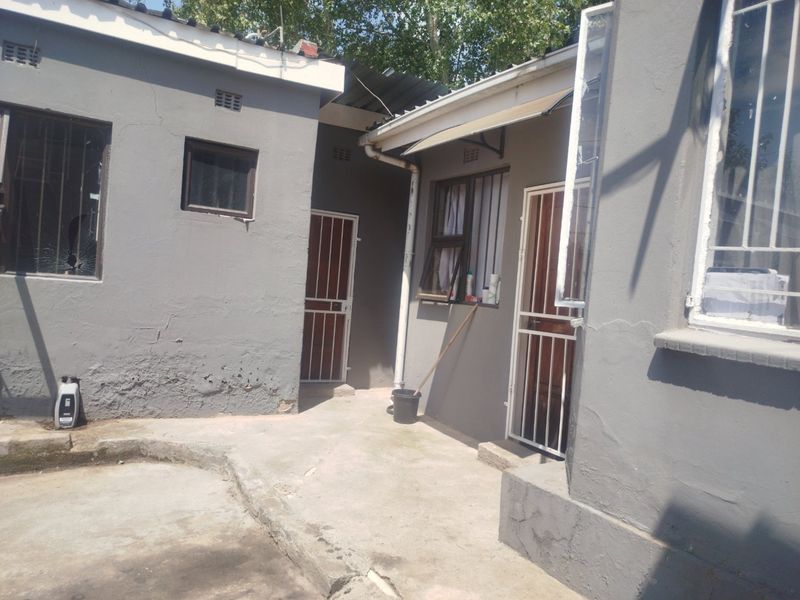Rear exterior view of the property showing concrete paving, security gates, and visible wear to the exterior wall plaster and paintwork.