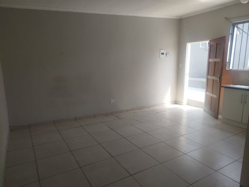 An empty open-plan living and kitchen area featuring tiled flooring, basic cabinetry, and direct access to an exterior space.