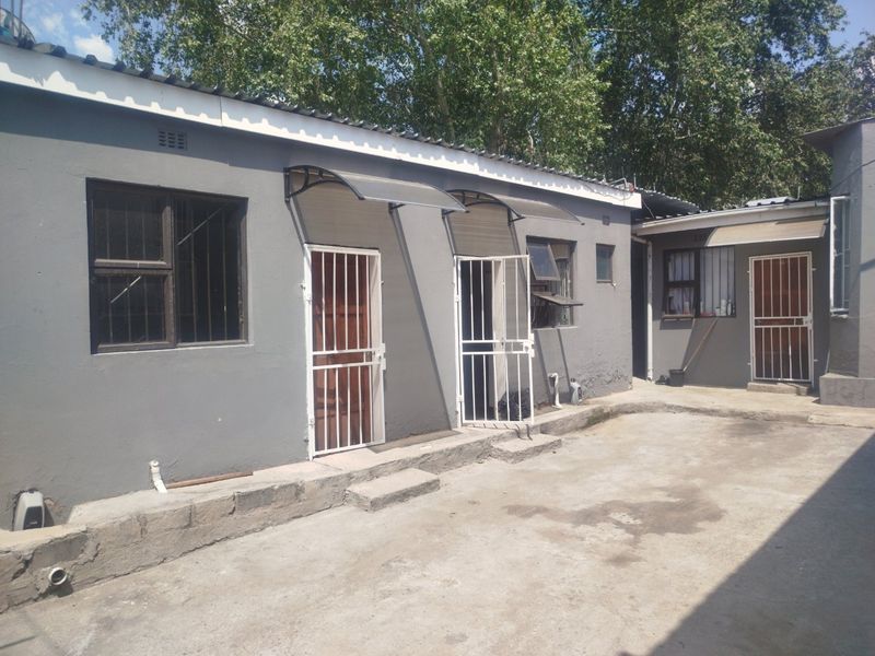 Rear exterior view of the property featuring multiple access points with security gates, concrete paving, and basic structural finishes.