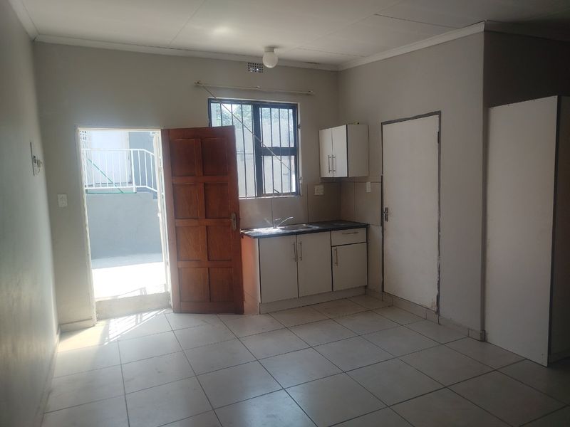 A compact, empty kitchen area featuring basic cabinetry, a sink, and tiled flooring, with direct access to an outdoor patio area.