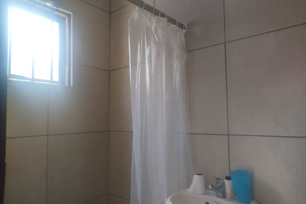 A functional bathroom featuring tiled walls, a wall-mounted basin with a chrome mixer tap, and a shower area with a curtain rail.