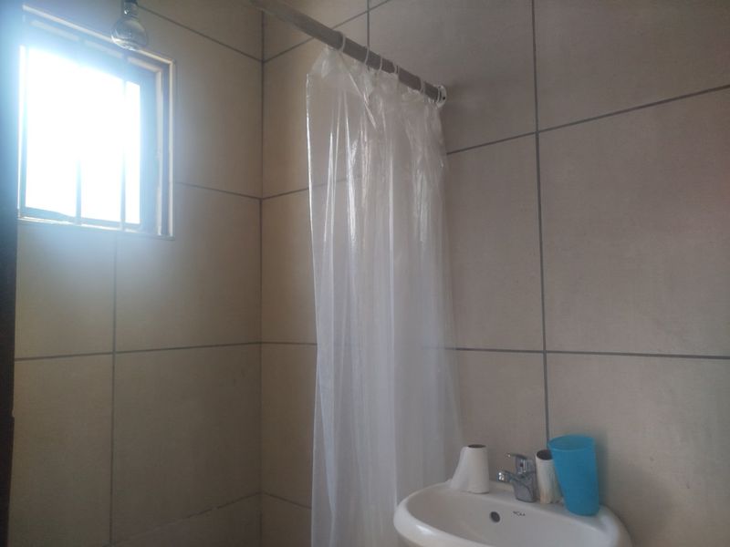 A functional bathroom featuring tiled walls, a wall-mounted basin with a chrome mixer tap, and a shower area with a curtain rail.