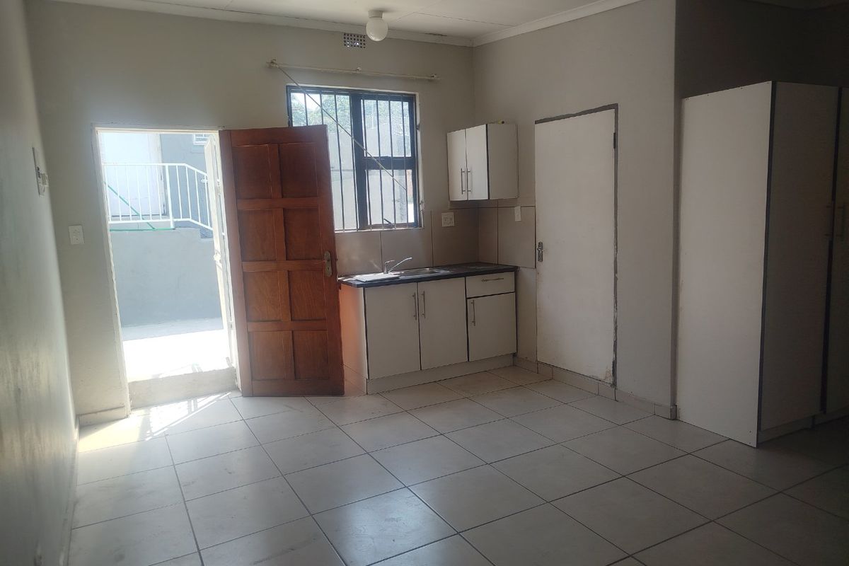 A compact, empty kitchen area featuring tiled flooring, basic cabinetry with a sink, and direct access to an outdoor space.