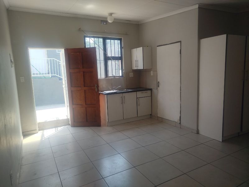 A compact, empty kitchen area featuring tiled flooring, basic cabinetry with a sink, and direct access to an outdoor space.