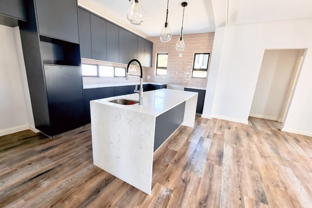 Modern kitchen featuring dark cabinetry, a central island with a quartz countertop, subway tile backsplash, and wood-look flooring in an open-plan layout.