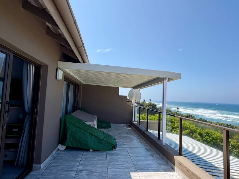 Spacious balcony featuring tiled flooring, a modern louvred roof, and a glass balustrade, offering expansive ocean views.