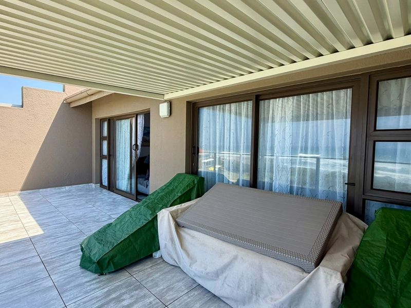 A spacious covered balcony featuring tiled flooring and large sliding glass doors, offering an ideal outdoor area for relaxation.