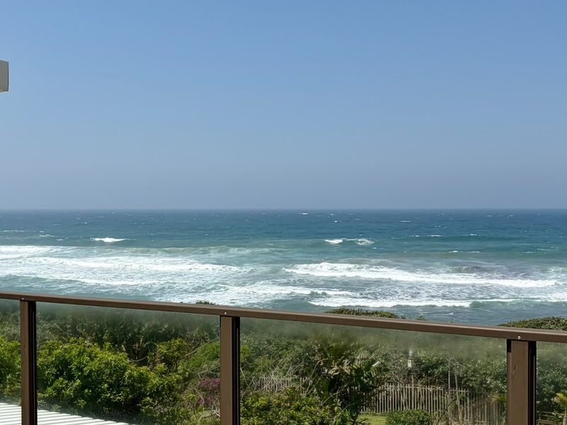 A clear, elevated view of the ocean from a balcony featuring a modern glass balustrade.