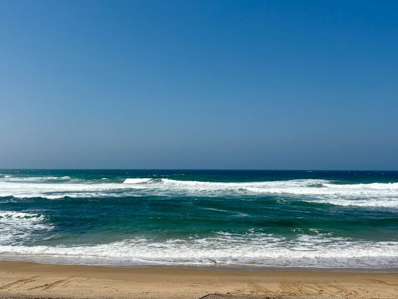 A scenic view of the ocean waves crashing onto the sandy beach.