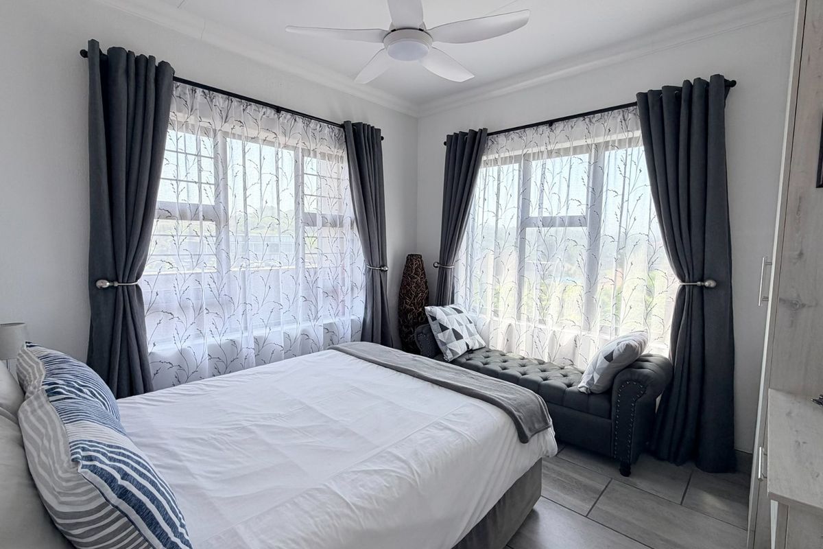 A bright and well-maintained bedroom featuring tiled flooring, a ceiling fan, and large windows that provide ample natural light.