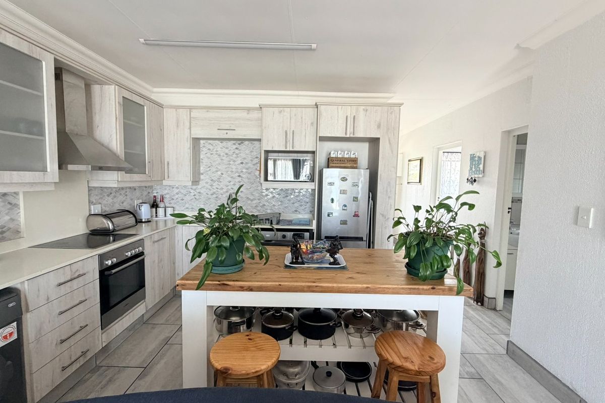 A well-maintained kitchen featuring light wood-grain cabinetry, a tiled backsplash, built-in oven and hob, and a central island with integrated storage.