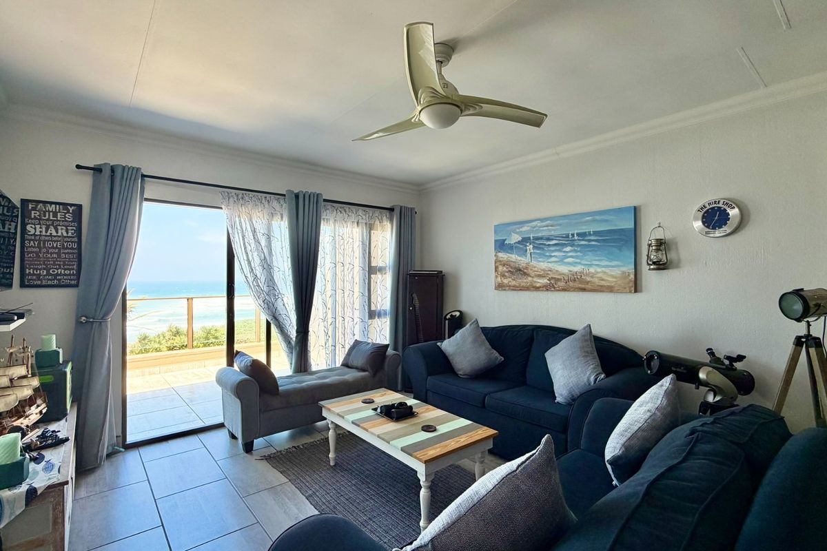A bright living room featuring tiled flooring, a ceiling fan, and large sliding glass doors that open onto a balcony with ocean views.