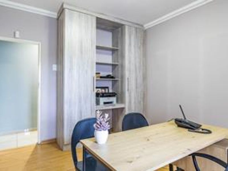 A functional home office featuring light wood-look laminate flooring and integrated built-in cabinetry with open shelving.