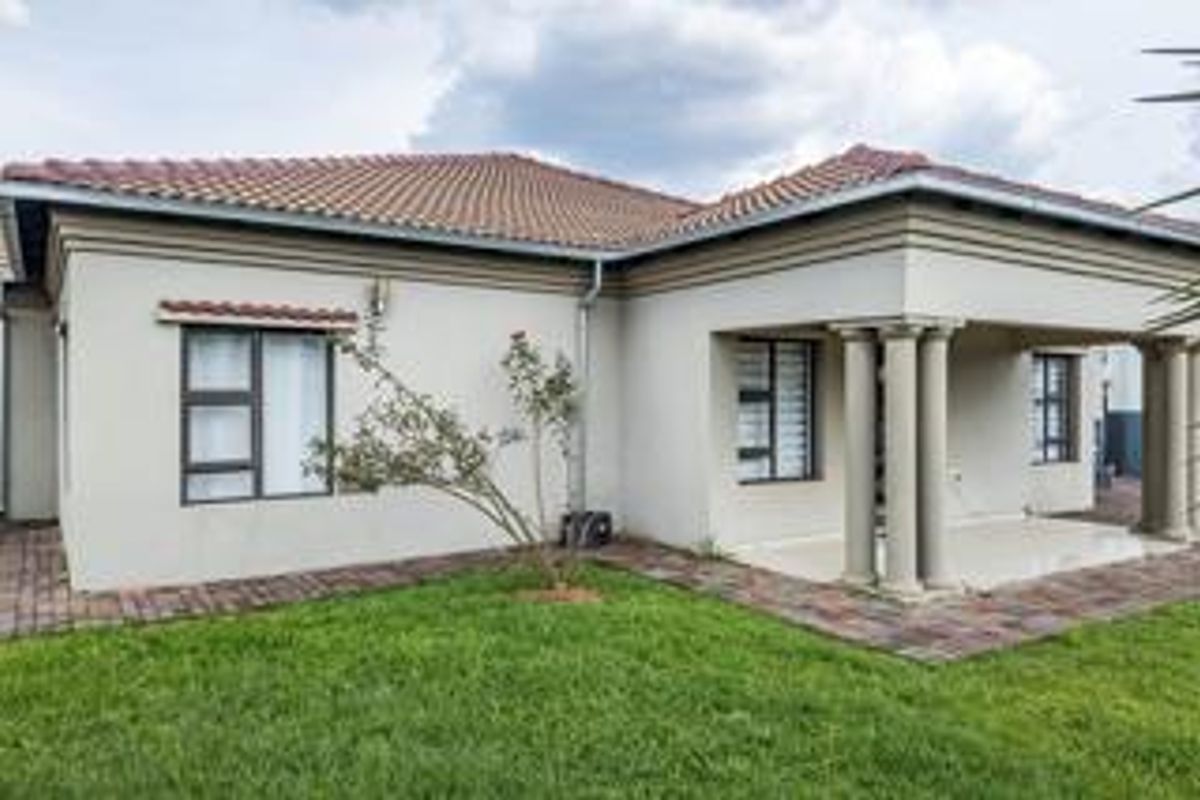 Rear view of the house featuring a covered patio with concrete columns, tiled roof, and paved walkway surrounding the lawn.