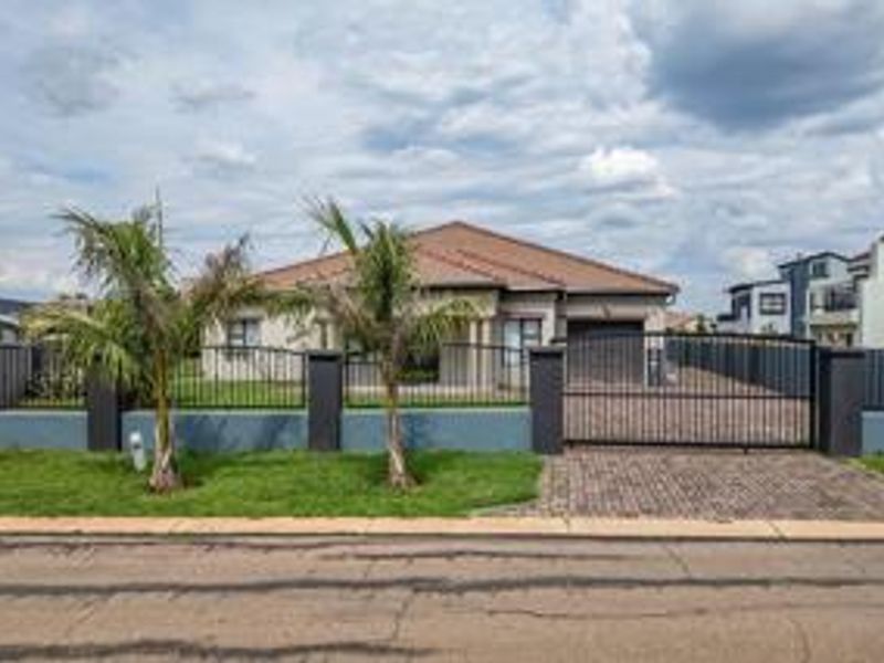 Front elevation of a single-story house featuring a tiled roof, paved driveway, and secure metal perimeter fencing with a sliding gate.