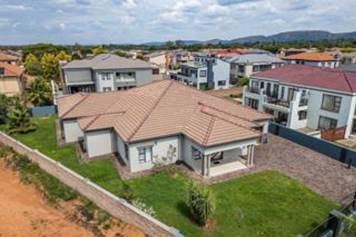 Aerial view of a modern residential property featuring a tiled roof, paved driveway, and a covered patio set within a landscaped garden.