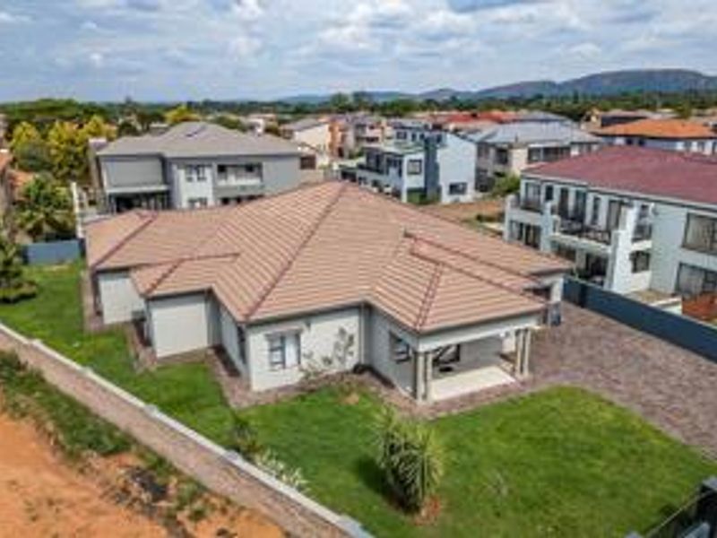 Aerial view of a modern residential property featuring a tiled roof, paved driveway, and a covered patio set within a landscaped garden.