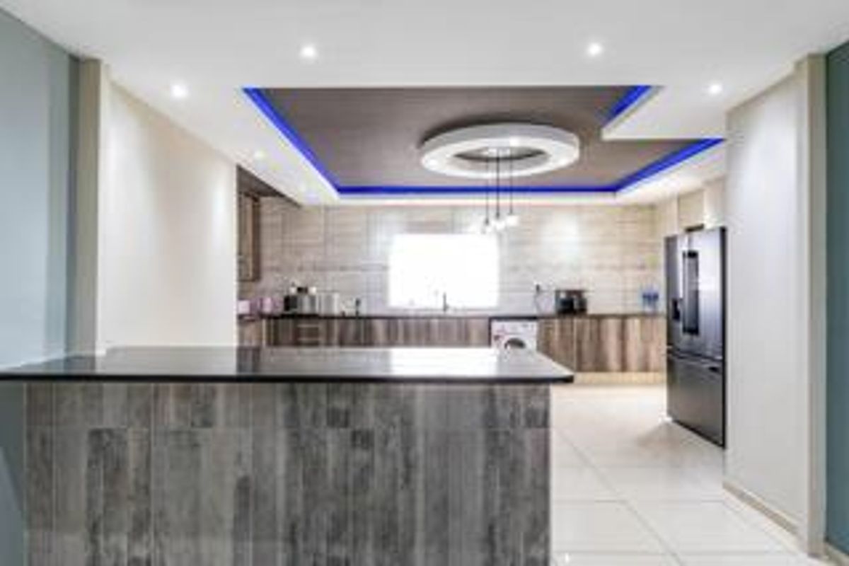 Modern kitchen featuring a central island with granite countertops, extensive built-in cabinetry, tiled backsplash, and a stylish drop ceiling with integrated lighting.