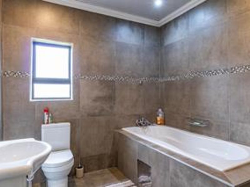 Modern bathroom featuring full-height grey wall tiling with decorative mosaic accents, a built-in bathtub, pedestal basin, and a dual-flush toilet.