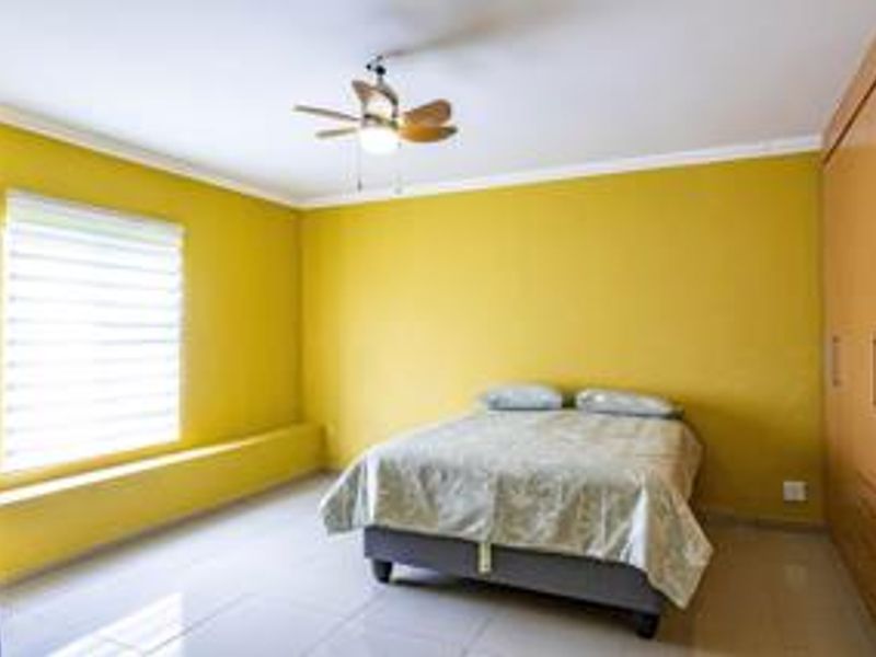 A bedroom featuring built-in cupboards, tiled flooring, a ceiling fan, and large windows with roller blinds.